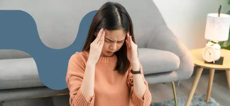 Mulher com as mãos na cabeça e expressão de dor de enxaqueca