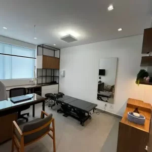 Consultório da Clínica Vertz Tatuapé com maca de quiropraxia, estação de atendimento, decoração moderna e iluminação natural para maior conforto dos pacientes.